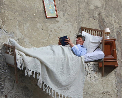 french artist thierry mandon reads in a bed dangling from abandoned building