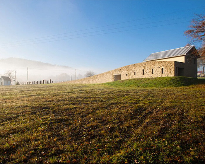 arched stone wall rises from the ground to embrace 'chapel of the last farewell' in poland