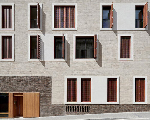 textured façades, wooden shutters and plinth detailing shape multi-dwelling building in barcelona