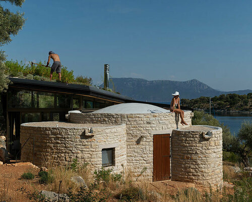 a cluster of curved stone volumes by hiboux architecture nestles in the rocky greek landscape