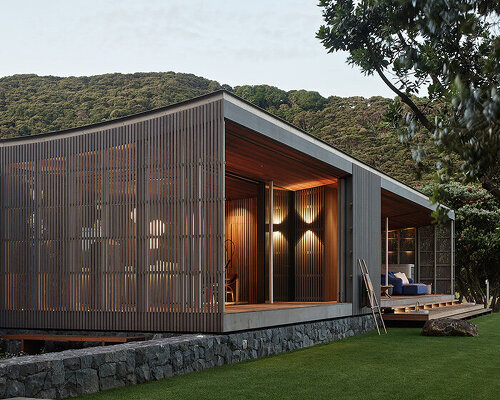 herbst architects' omata beach house glows through a timber screen in new zealand