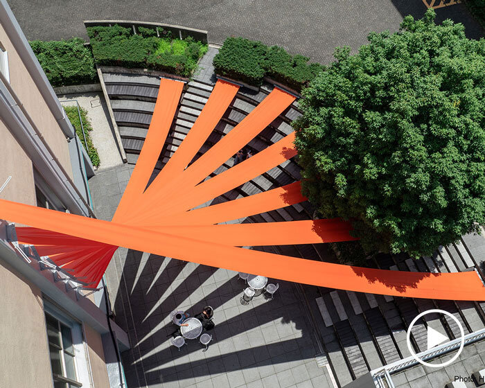 bright orange fabric panels fan out above university's terraced amphitheater in japan